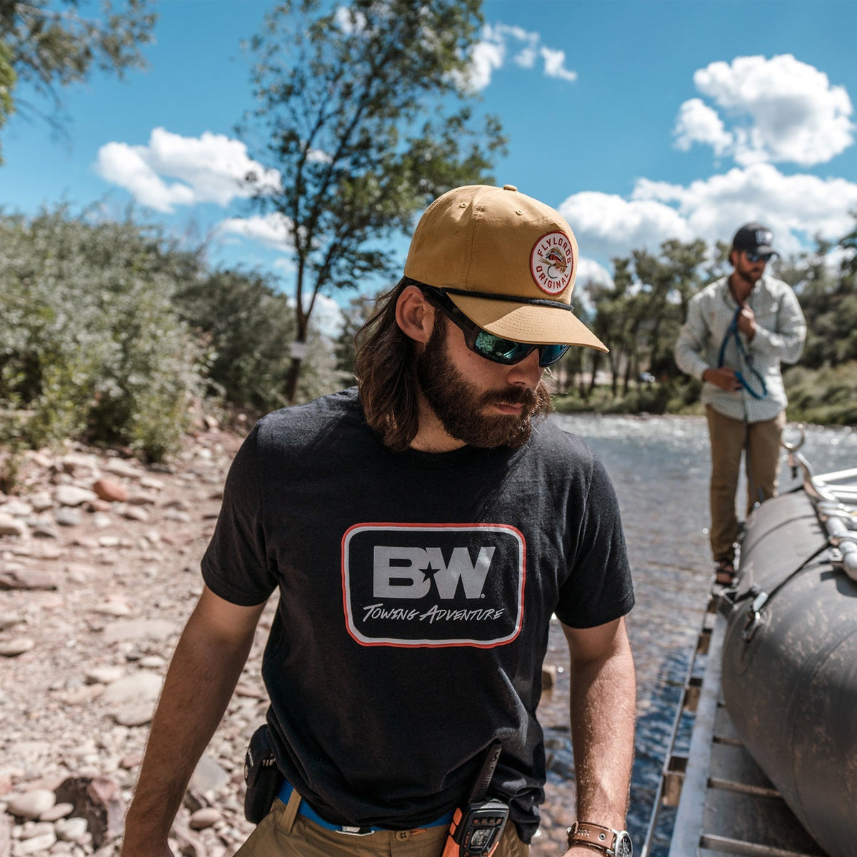 a fisherman wearing a b&w towing adventure tshirt walking alongside of his trailer and raft while at the river